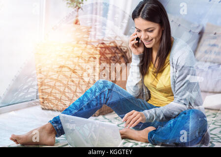 Freundliche junge Frau am Telefon zu sprechen, während zu Hause sitzen Stockfoto