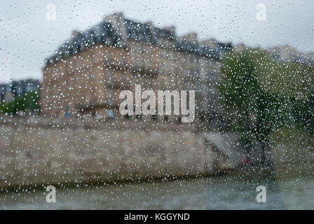 Regentag in Paris. Gebäude auf Abend-Flußdamm durch Regentropfen bedeckt Fenster gesehen. Stockfoto