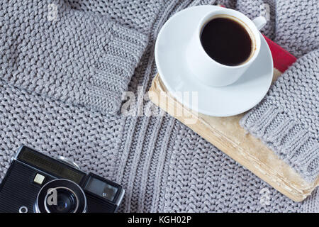 High-Angle Shot eine weiße Keramiktasse mit weißen Kaffee, Buch und eine alte Kamera von einem Pullover Stockfoto