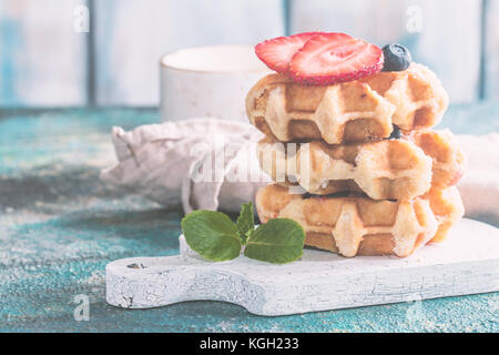 Stapel mit hausgemachten belgischen Waffeln mit Erdbeeren, Blaubeeren und Sirup auf blauen Tabelle Stockfoto