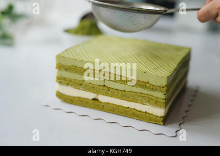 Grüner Tee Pulver über leckeren Käsekuchen gießen Stockfoto