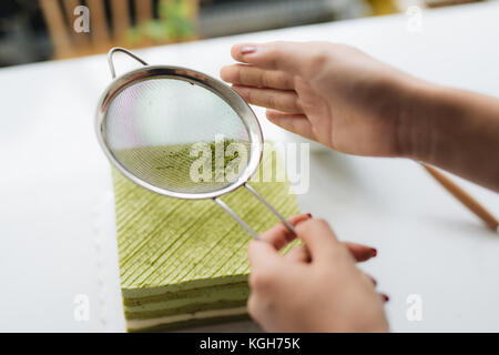 Grüner Tee Pulver über leckeren Käsekuchen gießen Stockfoto