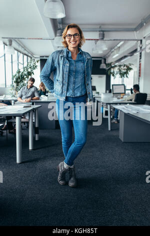 Junge weibliche Manager stehen im Büro mit den Kollegen im Hintergrund arbeiten. Happy Geschäftsfrau in die Kamera schauen und lächeln. Stockfoto