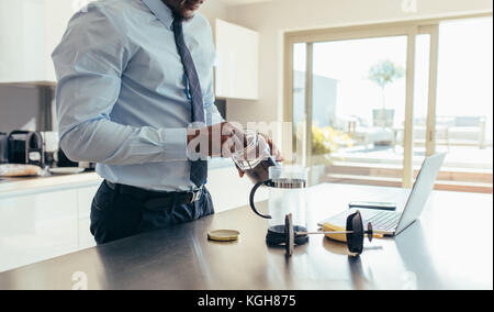 Mann in formelle Kleidung Kaffee mit französischen Presse mit einem Laptop am Küchentisch. Geschäftsmann Kaffee vorbereiten, während Sie im Büro arbeiten, um eine Stockfoto