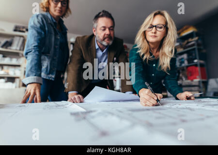 Business Team diskutiert über Fehler im Projekt. Drei Geschäftsleute, die sich einen Bauplan ansehen. Stockfoto