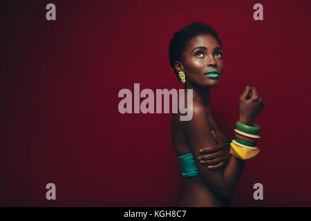 Attraktive junge afrikanische Frau mit lebendigen Make-up. Beauty Portrait von weiblichen Modell mit lebendigen Make-up auf roten Hintergrund. Stockfoto