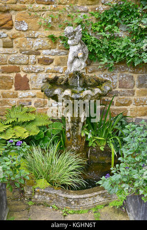 Eine kleine dekorative Garten Brunnen mit Putto mit Gräser und Farne Stockfoto