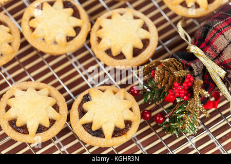 Frisch gebackene Mini Star überstieg Mince Pies auf einem Gitter mit einem weihnachtlichen Acorn und Berry Anordnung Stockfoto