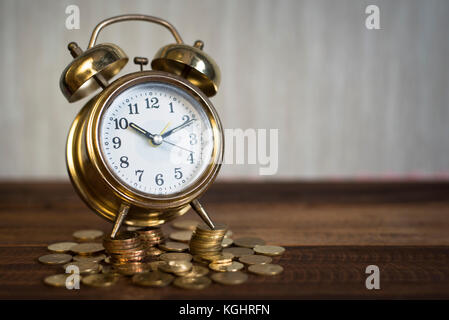 Zeit ist kostbar Konzept - Golden Bell Uhr mit Münzen auf einem Holztisch Hintergrund Stockfoto