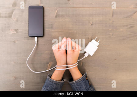 Weibliche Hände und Smartphone. Woman's Händen gefangen und der Handgelenke mit Handy Kabel wie Handschellen gewickelt. Neigung zu Internet und soziale Netzwer Stockfoto