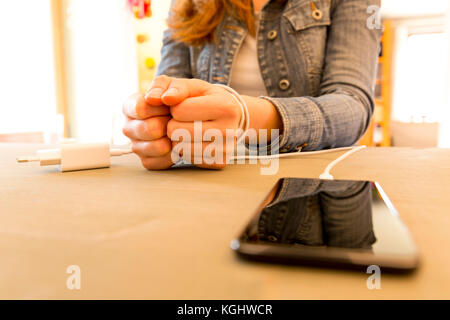 Weibliche Hände und Smartphone. Woman's Händen gefangen und der Handgelenke mit Handy Kabel wie Handschellen gewickelt. Neigung zum Internet und soziale Netzwer Stockfoto