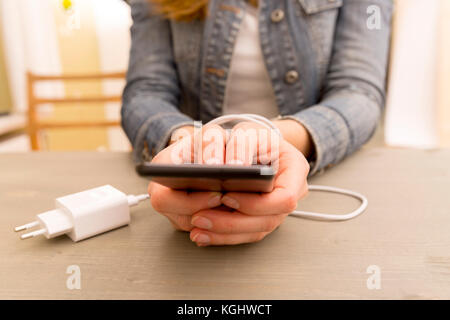 Weibliche Hände und Smartphone. Woman's Händen gefangen und der Handgelenke mit Handy Kabel wie Handschellen gewickelt. Neigung zum Internet und soziale Netzwer Stockfoto