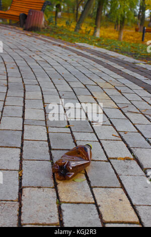 Eine komprimierte braune Plastikflasche lag auf Fliesen im Park. Abfälle im Stadtbild. Stockfoto