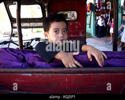 Antipolo City, Philippinen - November 3, 2017: Ein kleiner Junge, Lächeln für die Kamera, während auf der Rückseite einer geparkten Dreirad. Stockfoto