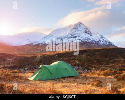 Grüne touristischen Zelt auf der Wiese am Fluss unter schneebedeckten Kegel von Berg Stob Dearg 1021 Meter hoch. Highland in Schottland einen wunderbaren sonnigen Tag. D Stockfoto