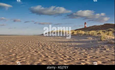 Menschenleeren Strand mit Leuchtturm hinter Sanddünen im Abendlicht in einem niedrigen Winkel sehen. Spuren im Sand Stockfoto