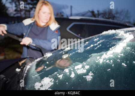 Frau kratzen Eis ihr Auto Windschutzscheibe am frühen Morgen mit einem Eiskratzer und die abgeschabte Eis aufgeschichtet auf Windschutzscheibe, flintshire, Wales, Großbritannien Stockfoto