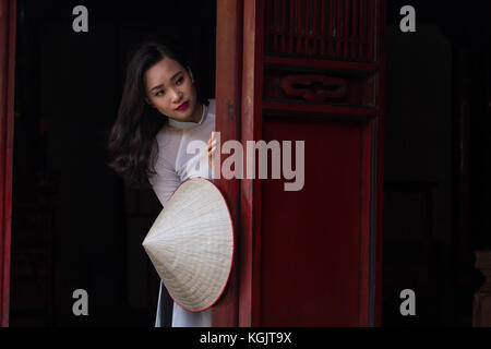 Eine junge Vietnamesin tragen die traditionelle Kleidung Ao Dai und der Konischen hat nicht La Lage; Tempel der Literatur in Hanoi, Vietnam Stockfoto