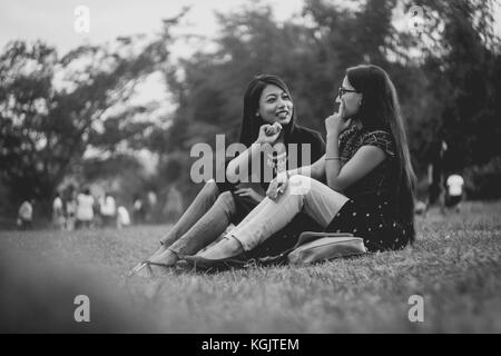 Zwei junge Mädchen, die einen sprechen, während Sie sitzen im Park von marngar See. Stockfoto