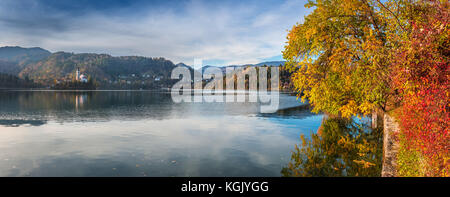 Bled, Slowenien - Panoramablick auf die schönen Herbstfarben am Bleder See mit Wallfahrtskirche Mariä Himmelfahrt und Bäumen Stockfoto