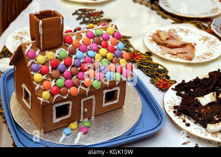 Traditionelle festliche Gingerbread House auf eine Tabelle mit den Überresten der Weihnachtsessen und Pudding Stockfoto