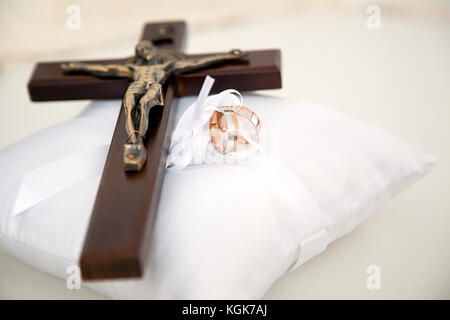 Hochzeit Ringe und kleine Holz- christliche Kreuz mit Christus auf weißen dekorative Kissen gelegt.jpg Stockfoto