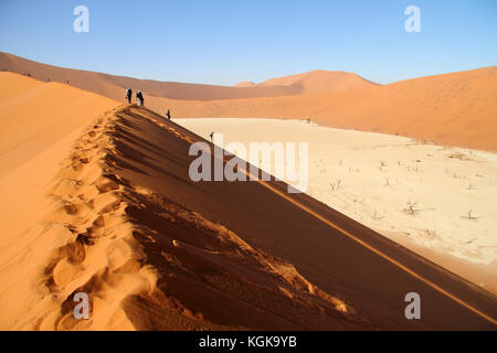 Touristische gehen bis eine rote Düne in sossuslvei mit Blick auf deadvlei, Namib Naukluft National Park, Wüste Namib, Namibia. Stockfoto