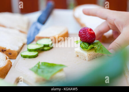 Geschnittenes Brot mit Frischkäse, frischen Spinat Blatt und eine ganze Erdbeere, auf einem Tisch platziert, auf Schneidebrett, im Freien. Boy' s vor PICKIN Stockfoto