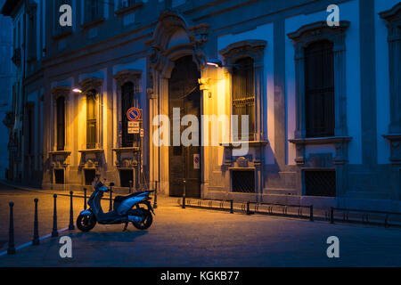 Heitere Sicht auf ein kleines Motorrad in einer Gasse in Mailand, Italien geparkt, in der Nacht, unter der warmen Farbe der Straße Licht Stockfoto