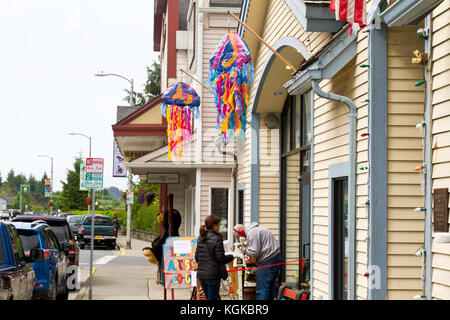 Eine Frauen touristische beobachtet einen Mann an einem Holz Drehbank außerhalb ein Shop in Sitka, Alaska. Stockfoto