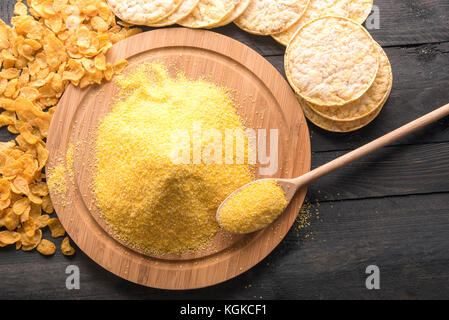 Hohe Betrachtungswinkel und einer runden Platte voller Mais Mehl, durch Produkte aus it, Corn Flakes und Gepuffter mais Kuchen umgeben, auf einem schwarzen Holz- ta Stockfoto