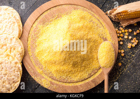 Oben Ansicht mit Mais Mehl auf einer runden Platte für Mais Kuchen, Maiskolben und Körner umgeben, auf einem vintage Tabelle. Stockfoto