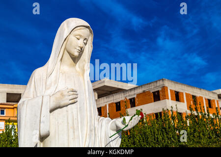 Statue der Muttergottes von Medjugorje, der seligen Jungfrau Maria, am blauen Himmel und unter dem Bau von Häusern Stockfoto