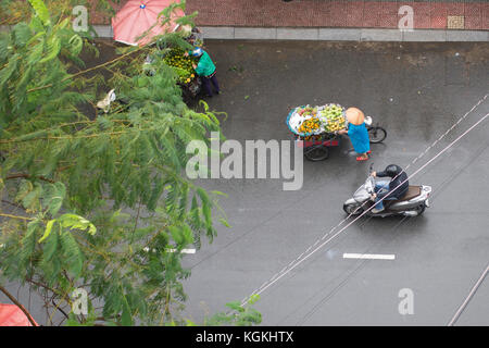 Luftaufnahme von einen Menschen auf den Roller und ein Verkäufer mit typischen vietnamesischen konischen Hüten und seine Barrow Spaziergänge durch die Straßen von Hanoi in Vietnam duri Stockfoto