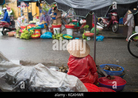 - Selektiver Fokus - nicht identifizierte Frau mit typischen vietnamesischen konischen Hüten verkaufen frisches Gemüse auf einem Straßenmarkt in Hoi An, Vietnam Stockfoto