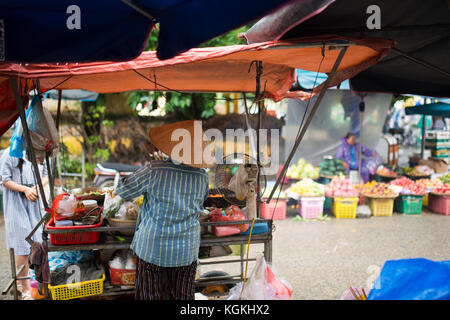 - Selektiver Fokus - nicht identifizierte Frau mit typischen vietnamesischen konischen Hüten verkaufen frisches Gemüse und Fleisch Spieße auf einem Straßenmarkt in Hoi An, Vietnam Stockfoto