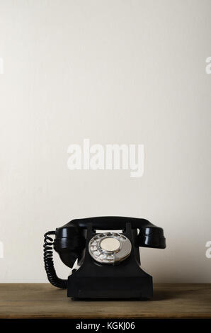 Schwarz 1940s Vintage Bakelit Telefon auf einem Schreibtisch aus Holz mit Elfenbein weiße Wand als Hintergrund für die Bereitstellung von oben kopieren. Stockfoto