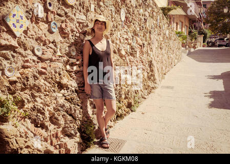 Italienische Sommerferien: Frau touristische Tragen hat alleine stehen neben einer alten Steinmauer in einer kleinen Straße in einem alten Dorf in der Toskana, Italien Stockfoto