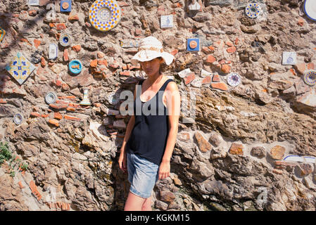 Italienische Sommerferien: Frau touristische Tragen hat alleine stehen neben einer alten Steinmauer in einer kleinen Straße in einem alten Dorf in Sizilien, Italien Stockfoto