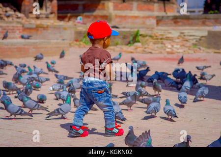 Kathmandu, Nepal - April 26, 2012: Unbekannter kleine schwarze Kind zu Fuß auf der Straße mit einem Schwarm Tauben, am Durbar Square in der Nähe von Alte hinduistische Tempel in Kathmandu, Nepal Stockfoto