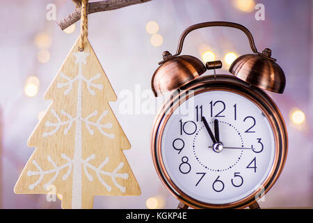 Vintage Kupfer Wecker mit fünf Minuten bis Mitternacht. Silvester Countdown. Holz Christbaumschmuck hängt am Zweig. glitzernde Girlanden li Stockfoto