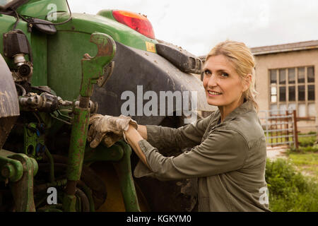 Portrait von lächelnden Frau Bauer von landwirtschaftlichen Maschinen gegen Sky Stockfoto