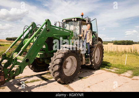 Volle Länge des lächelnden reife Frau steht auf landwirtschaftliche Maschinen gegen Sky Stockfoto