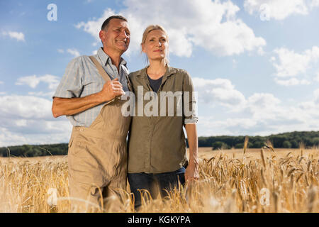 Low Angle View von Reifes Paar steht man inmitten Nutzpflanzen der Farm gegen Himmel an einem sonnigen Tag Stockfoto
