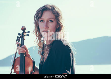 Portrait von selbstbewussten jungen Frau mit Geige gegen den klaren Himmel an einem sonnigen Tag Stockfoto