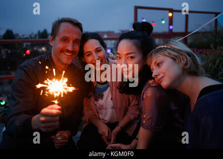 Portrait von glücklichen Mann mit Wunderkerzen beim Sitzen mit weiblichen Freunde bei Nacht Stockfoto