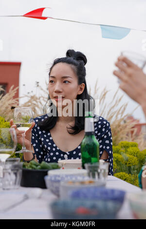 Nachdenkliche junge Frau mit Weinglas bei Tisch im Freien während der Partei sitzen Stockfoto