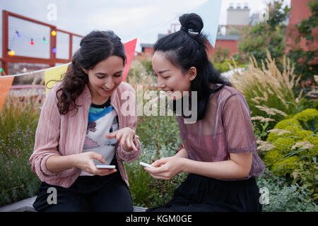 Gerne weibliche Freunde mithilfe von Smart Phones, beim Sitzen auf der Terrasse Stockfoto