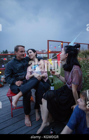 Glückliches Paar sprechen beim Sitzen mit Freunden auf der Terrasse in der Dämmerung Stockfoto
