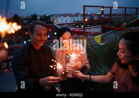 Männliche und weibliche Freunde holding Wunderkerzen auf der Terrasse Stockfoto